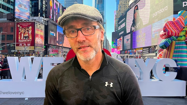 Un homme regarde la caméra avec, derrière lui, le décor de Times Square, à Manhattan.