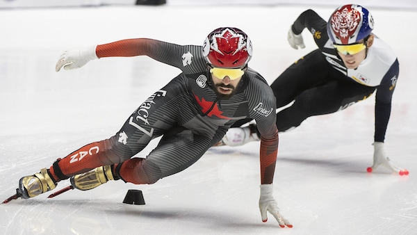 Steven Dubois pose la main gauche sur la glace, dans un virage, alors qu'un rival coréen le suit de près. 