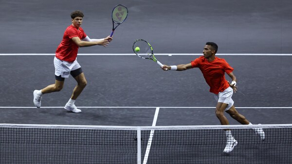 Félix Auger-Aliassime frappe la balle et son coéquipier Ben Shelton est en position à l'arrière-plan.