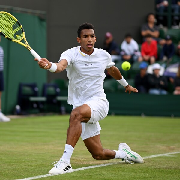 Vêtu de blanc, un joueur de tennis tente de frapper une balle sur un terrain de gazon.