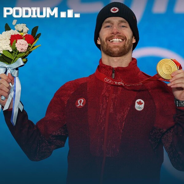Un athlète sourit et brandit sa médaille d'or.