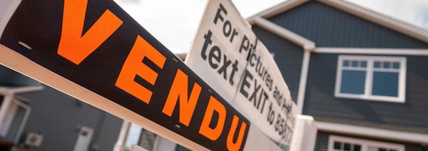 Affiche noire sur laquelle est écrit le mot «Vendu» en lettres orange devant une maison.