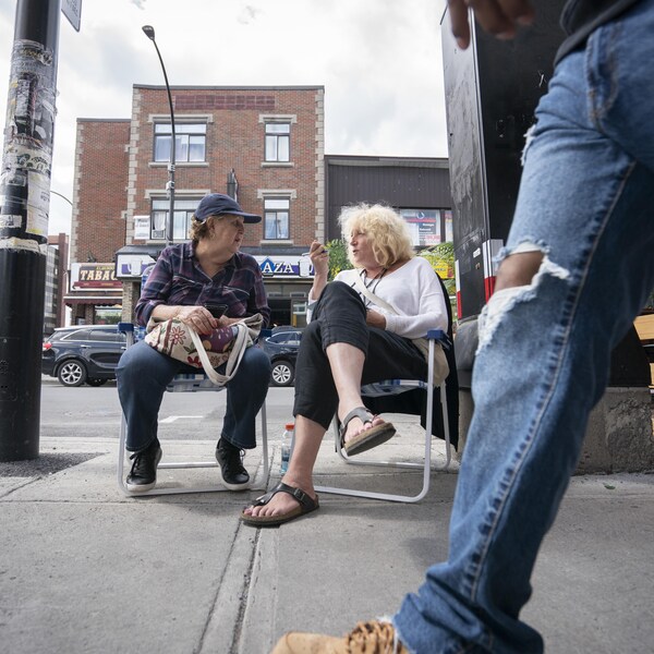 Deux femmes discutent assises sur des chaises, au beau milieu du trottoir.