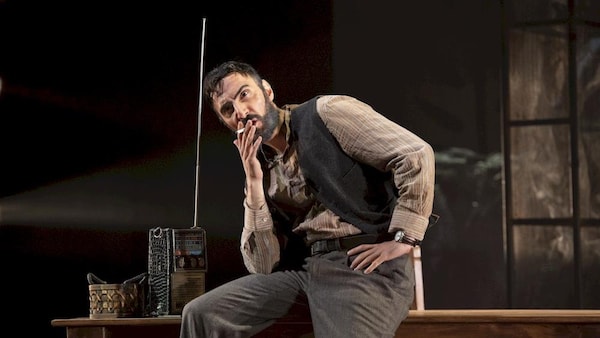 Un homme est assis sur le coin d'une table et il fume une cigarette.