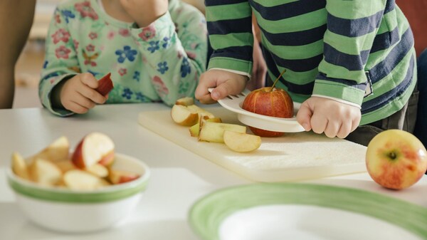 Deux enfants coupent des pommes sur une table. 