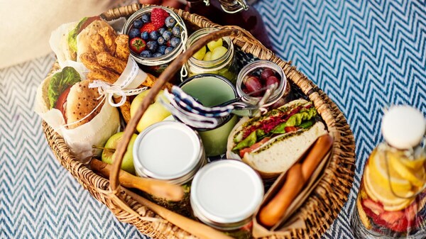 Gros plan sur un panier d'osier rempli de sandwichs, fruits, craquelins et bouteilles d'eau et de jus.