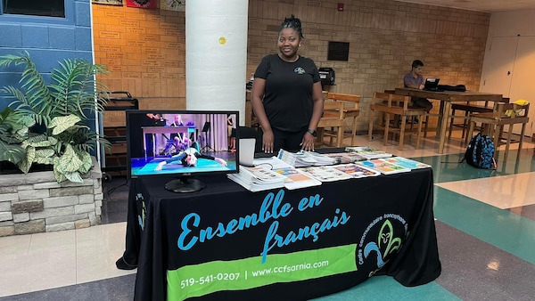 Nivelle Foueze derrière une table du Centre communautaire francophone de Sarnia avec des dépliants et autres brochures.