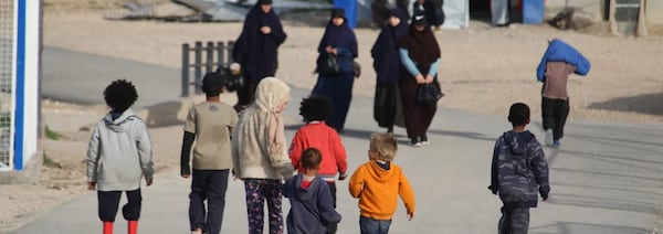 Des femmes voilés et des enfants marchent sur une route à l'intérieur d'un camp de détention. 