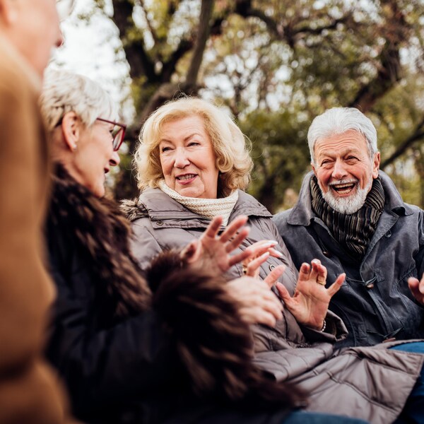 Deux couples de personnes âgées discutent sur un banc de parc.