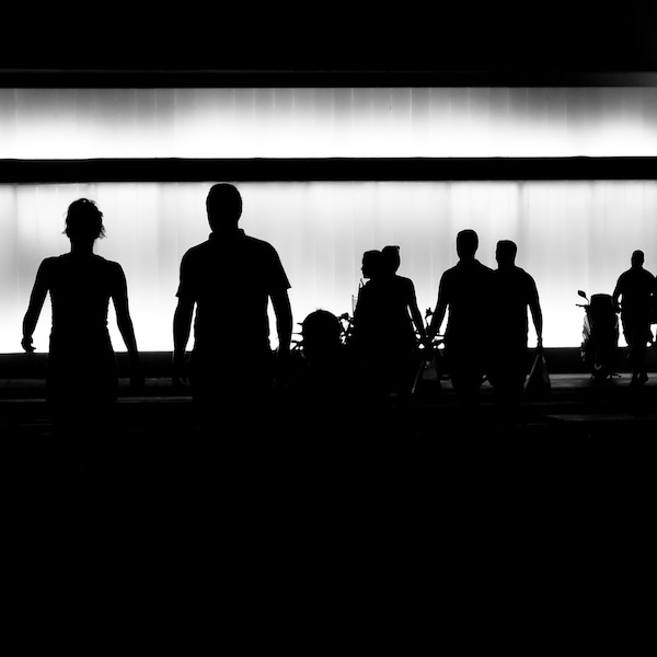 Image en noir et blanc montrant des silhouettes de personnes marchant dans une rue.
