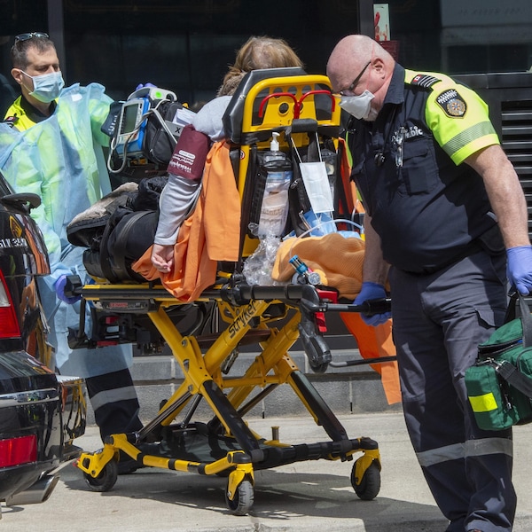 Des ambulanciers équipés de masques et de gants évacuent une patiente installée sur un brancard.