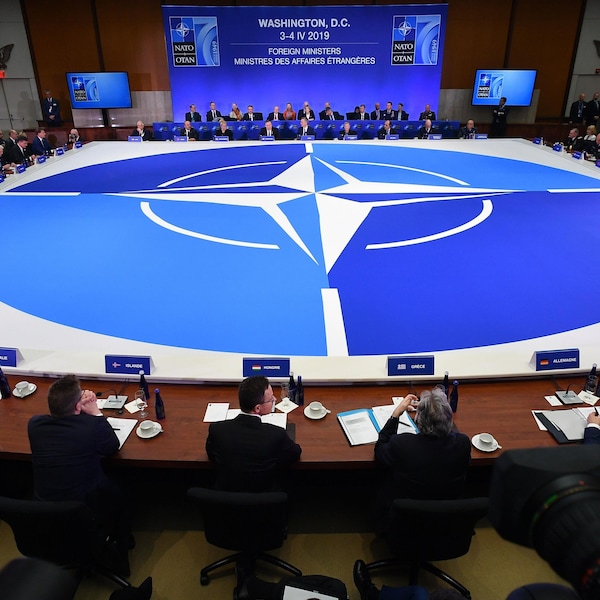 Des représentants des membres de l'OTAN assis à une énorme table sur laquelle le logo de l'organisation est mis à l'honneur. 