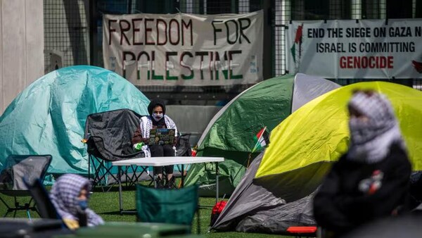 Des tentes, des chaises et des tables sont installés sur un terrain de gazon artificiel avec des banderoles en support de la Palestine.  