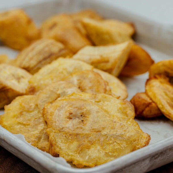 Des morceaux de bananes plantains frites jonchent une plaque à cuisson.