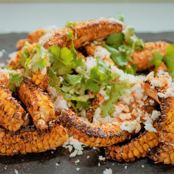 Des maïs grillé avec du feta et de la coriandre sur une plaque en ardoise. 