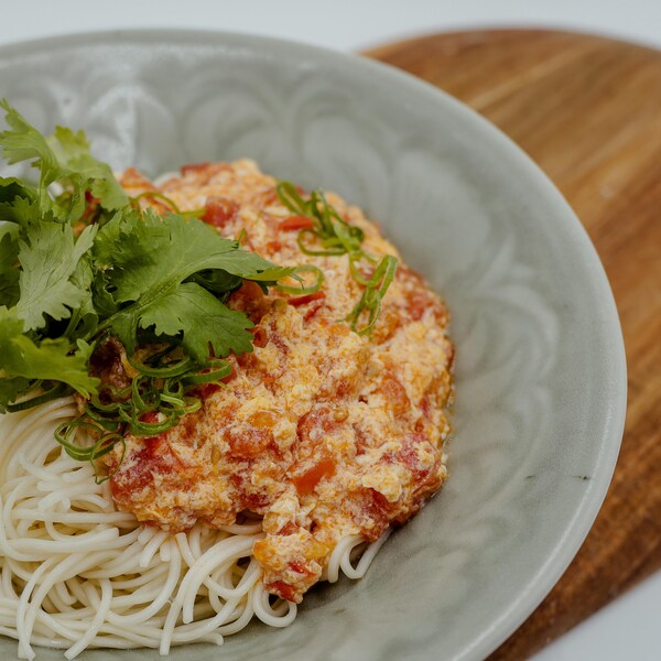 Une assiette plein de nouilles fines et un compoté de tomates sur le dessus. 