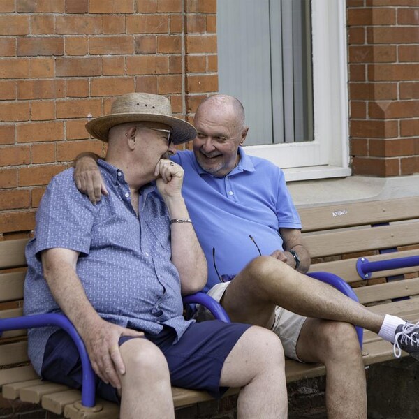 Deux hommes assis sur un banc se prennent dans leurs bras.
