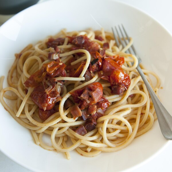Un bol de spaghettis avec des tomates cuites au four et de la chair de saucisses.