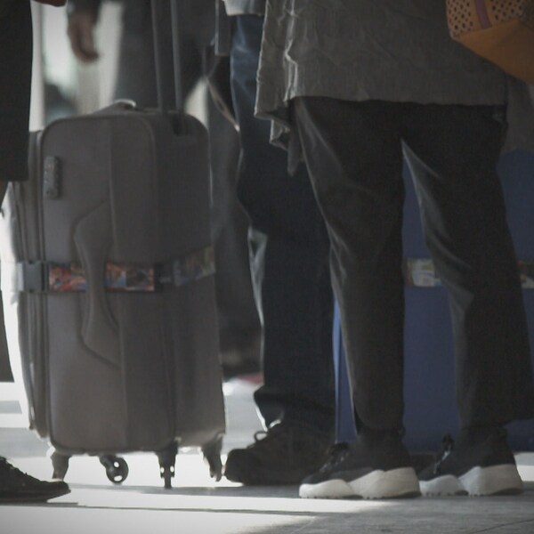 Des valises et les jambes de voyageurs qui attendent leur vol à l'aéroport de Montréal.