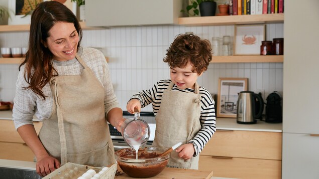 Une maman et son enfant préparent une recette dans la cuisine.