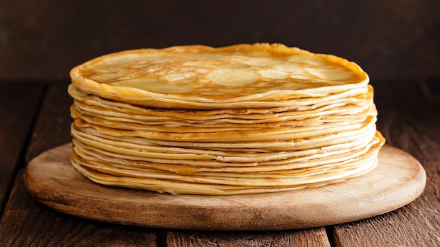 Une pile de crèpes minces sur une assiette de bois.