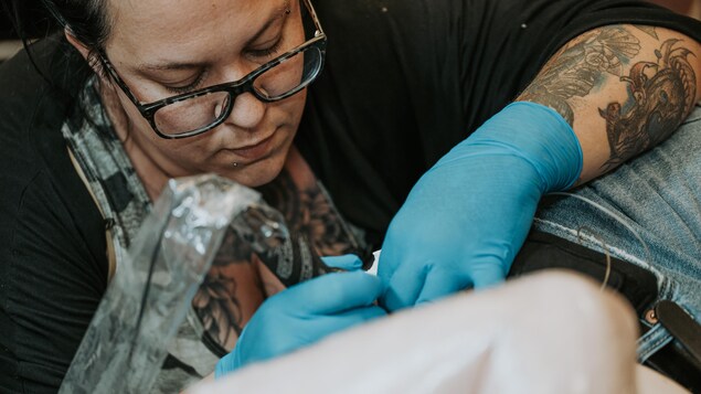 Elle est concentré et tatoue une cliente.
