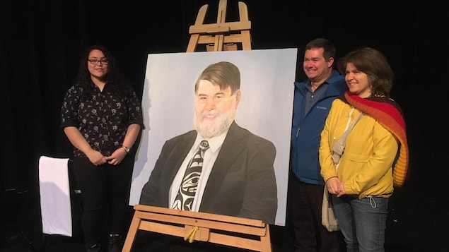 Trois personnes posent aux côtés d'une peinture représentant Bill Goodacre.