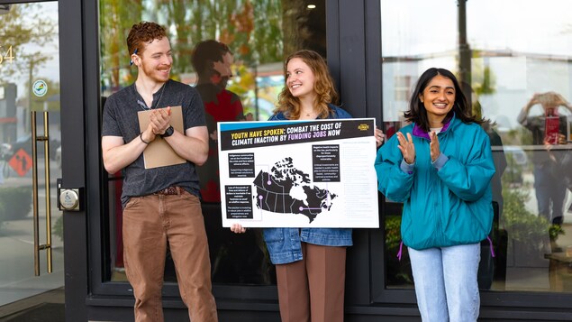 Trois jeunes sourient et portent un panneau avec une carte du Canada. Ils applaudissent aussi.