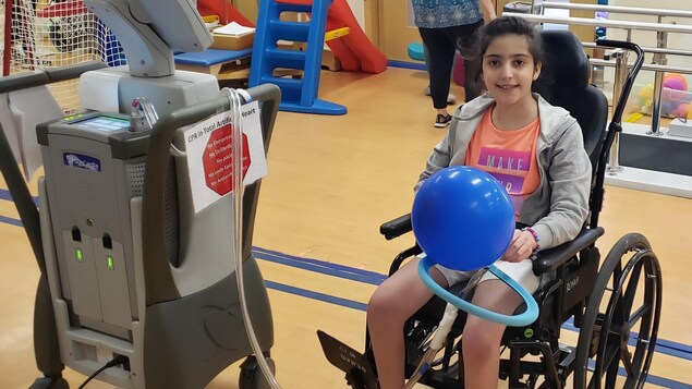 Mariam Tannous dans un fauteuil roulant branchée à une machine dans une chambre d'hôpital.