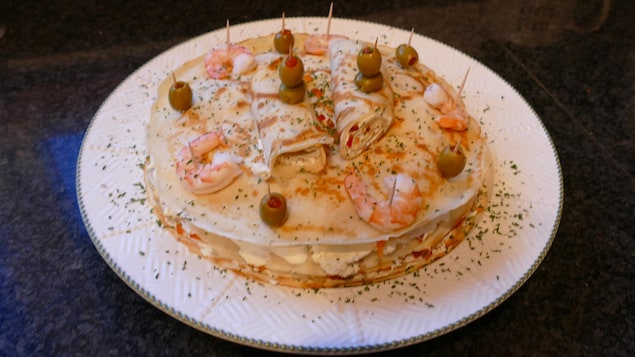 Dans une assiette, des crêpes superposées garnies de crevettes et olives.