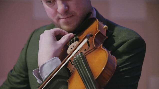 Un musicien tient un violon et un archet.