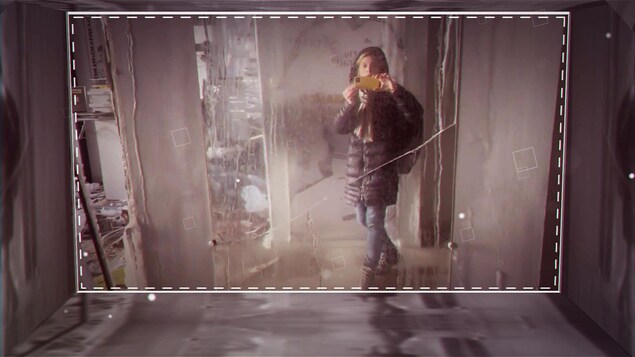Une femme filme avec son téléphone un endroit ravagé par les bombardements.