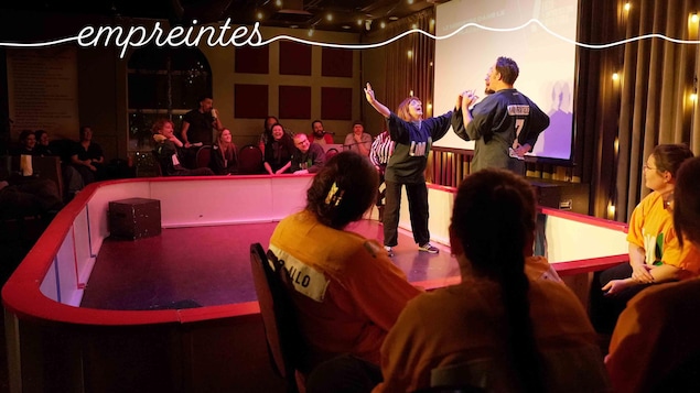 Deux improvisateurs sur une scène sombre, les bras levés en signe de victoire ou de joie intense. 