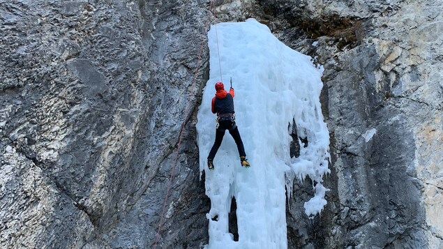 Un grimpeur escalade un mur de glace sur une falaise.