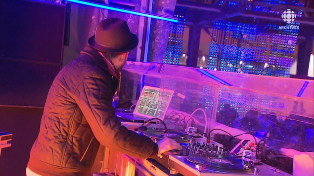 Un DJ jouant de ses tables tournantes devant un public à l'extérieur en hiver.