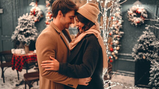 Un couple s'enlace en souriant devant un décor des Fêtes.