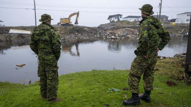 Deux militaires canadiens près de maisons endommagées.