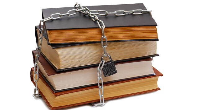 Une pile de livres est entourée d'une chaîne fermée par un cadenas.