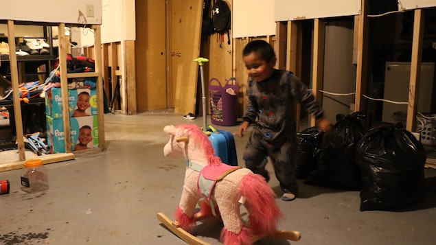 Un enfant joue devant un cheval rose et des sacs de poubelles et des paquets de couches.