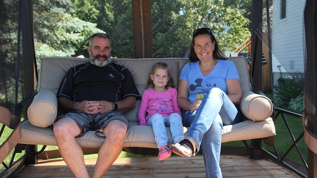 Une famille installée sur un canapé à balancement, devant leur maison.