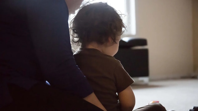 Une maman tenant son bébé dans ses bras.Ils sont assis de dos. 