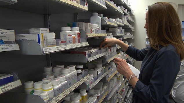 Une pharmacienne vérifie l'étiquette de flacons de médicaments sur une étagère.