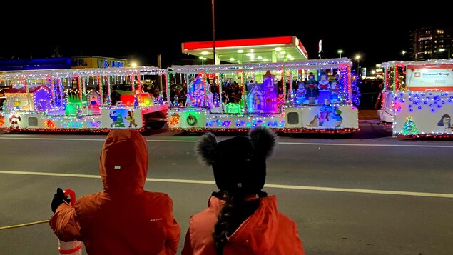 Deux enfants regardent un char allégorique de Noël. 