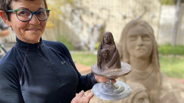 La sculptrice Patricia Leguen qui tient la maquette de sa sculpture qui représente une femme autochtone et son enfant. La sculpture en sable complétée est en arrière-plan.