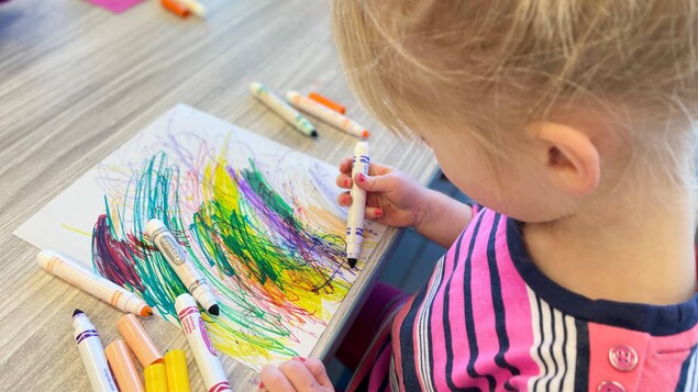 Une petite fille dessine avec des crayons-feutres.