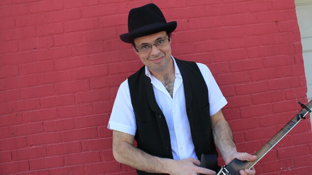 Leonard Podolak porte un chapeau et tient un instrument dans ses mains. 