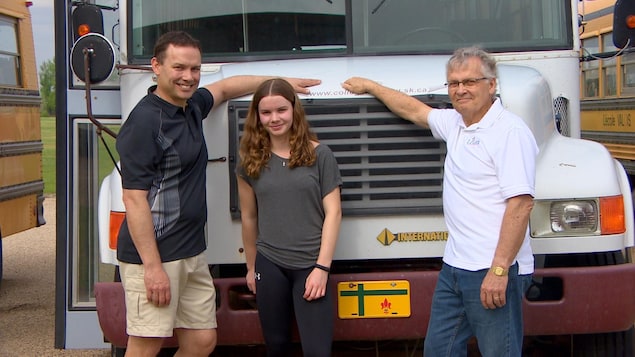 Deux hommes et une jeune femme devant un autobus, souriant. Ils sont tous de la même famille.