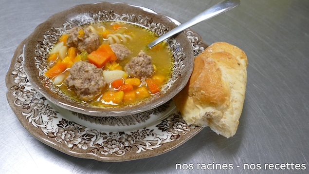La soupe aux boulettes et légumes dans un plat de service brun avec du pain croûté et ne cuillère.