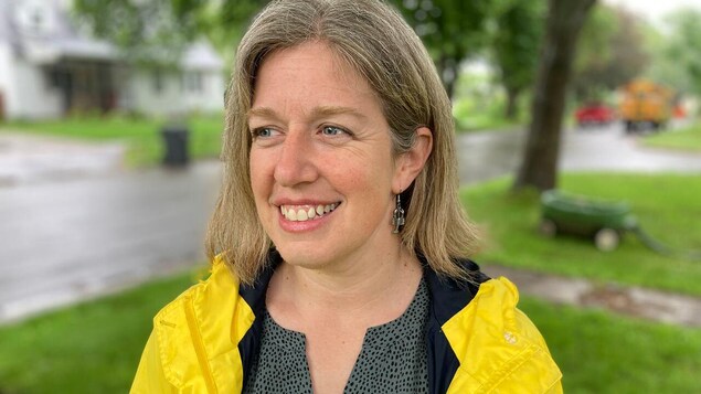 Susan Holt souriante, dehors et vêtue d'un imperméable jaune par une journée pluvieuse en été.
