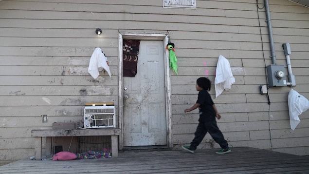 Un enfant marche vers la porte d'une résidence délabrée.
